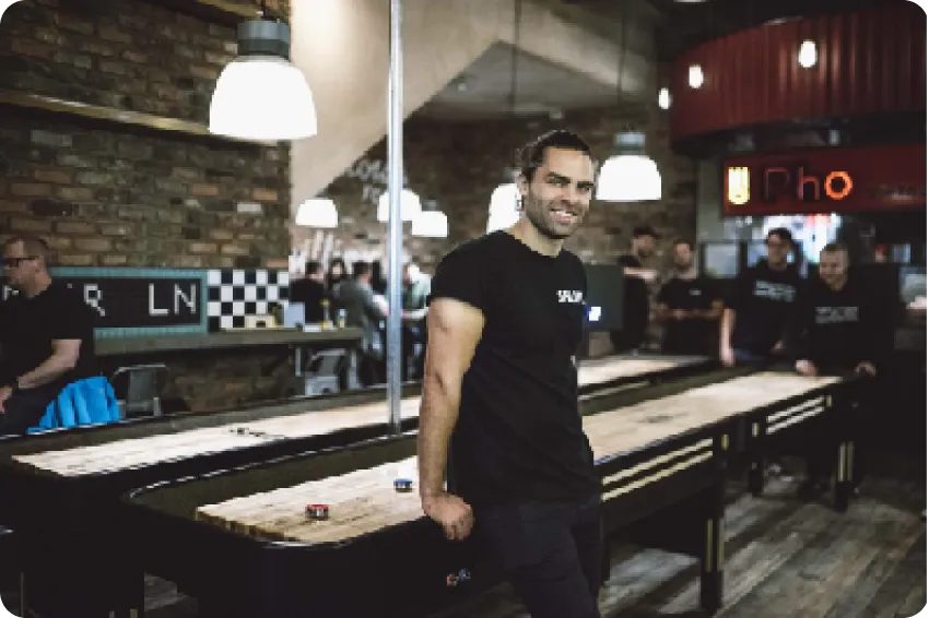 A member of the team standing beside a shuffleboard table in a busy venue